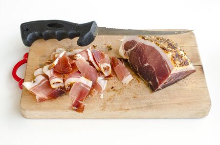 Homemade spicy prosciutto, smoked and dried in the wind for a long time, on wooden chopping board with long, thin knifeの写真素材