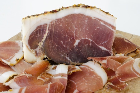 Homemade spicy prosciutto, smoked and dried in the wind for a long time on wooden chopping board, big piece and thin slices against white backgroundの写真素材