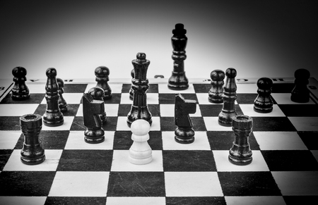 White pawn standing alone, surrounded by black chess figures, black & whiteの写真素材