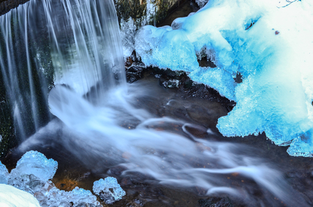 Detail of frozen brook - small waterfall, blue ice, stone, icicles and milky streamの写真素材