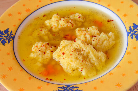 Homemade beef clear soup with dumplings served in yellow stylized plateの写真素材
