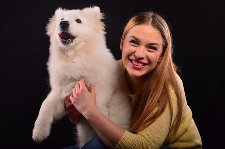 Young, cute blonde girl and Siberian samojed dog against black backgroundの写真素材