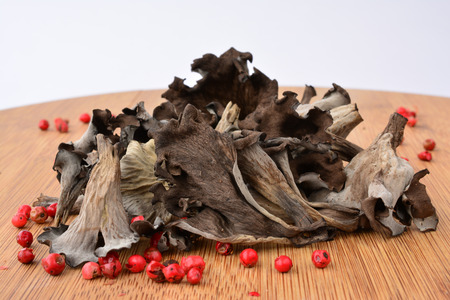 Pile of dried Horn of plenty or Craterellus cornucopioides mushrooms with spicy red pepper on bamboo wooden chopping board over white background, side viewの写真素材