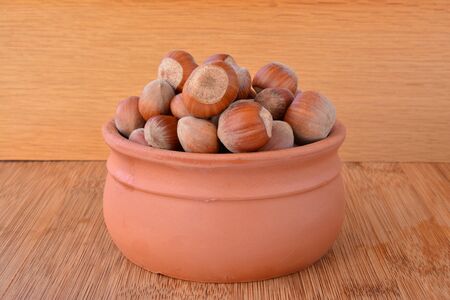 Fresh, tasty hazelnuts in small clay pot on wooden backgroundの写真素材