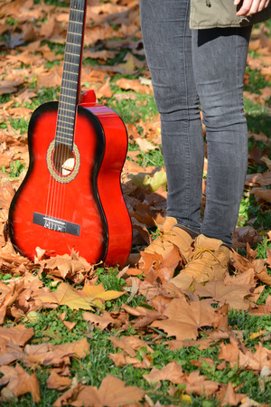 Legs and feet of young girl standing on lawn on lot of fallen leaves, wearnig jeans and warm autumn shoesの写真素材