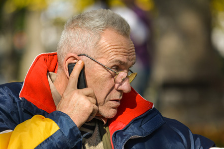 Good looking active senior concentrated on important news during phone call in bright, suuny autumn day, close up viewの写真素材