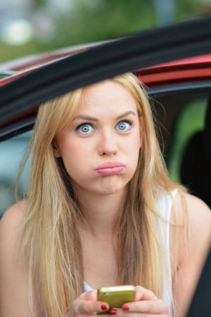 Young beautiful blonde girl sitting in a car and typing a message, looking tired and a little bit upsetの写真素材