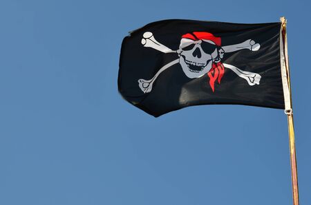 Pirate flag against clear,  blue sky fluttering in the wind, copy spaceの写真素材