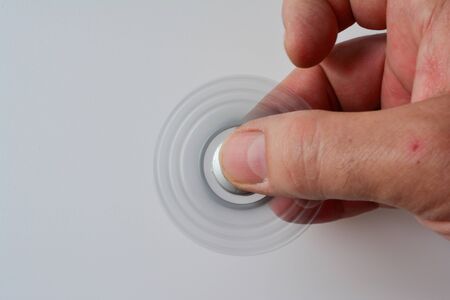 Silver fidget spinner in motion in man's hand over white background, copy space on left