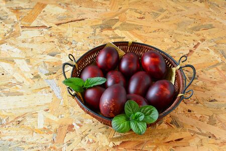 Lot of Easter eggs naturaly painted by onion shells in a wicker basket with some green plants, over wooden background, side and above viewの写真素材