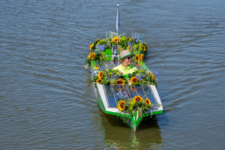 Boy with sunglasses in a small sunflowers boat powered on solar energy. Yearly parade of boats decorated with vegetables and flowers.のeditorial素材