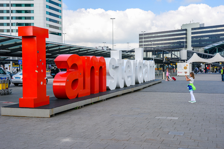 Amsterdam Airport, Schiphol, young female tourist takes a picture of the I Amsterdam sign in front of the passenger terminal of the airport.のeditorial素材