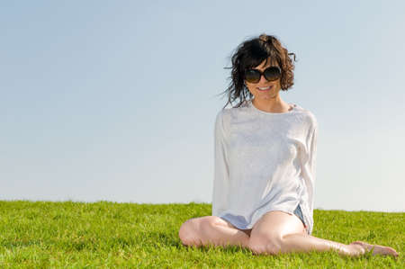 Smiling girl dressed in white sitting on the grass with blue skyの写真素材