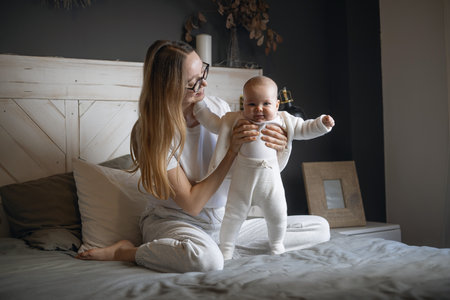 Beautiful mother with her baby. Young beautiful woman looks at her little daughter. Baby girl laughing in her mothers arms.の写真素材