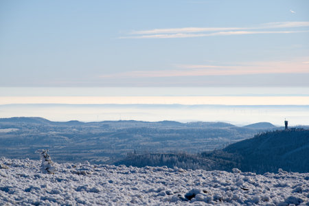 A wide landscape shot from a snowy peak showing layers of frosted hills, hazy valleys, and a tower on the distant horizon.の写真素材