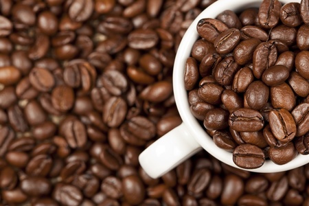 Espresso cup full with roasted cofee beans. In background are further cofee beans visible.