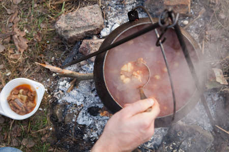 Cooking bogracs gulyas soup in a cauldron on fire in forestの写真素材