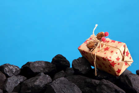 The package with the wrapped gift lies on a heap of black coal.の写真素材