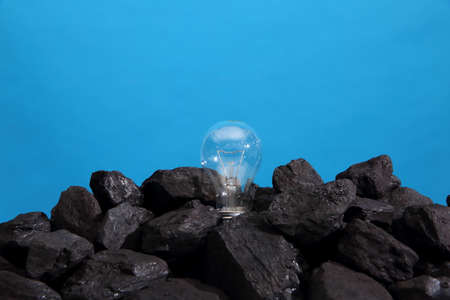 Black coal with a lighted bulb. On a blue background.の写真素材