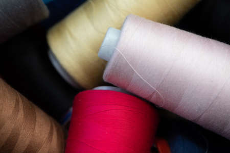 Different thread colors on large bobbins scattered randomly in a box ready to put on the sewing machine.の写真素材