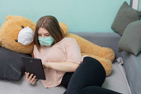 A teenager with her beloved plush companion tries to study for the matriculation examination. Together they are wearing protective masks.の写真素材