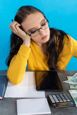While counting money, a young woman uses a calculator and a tablet to check the stock exchange.の写真素材