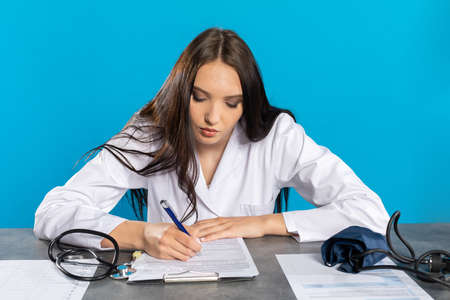A young lady doctor writes the test results to the patient's card.