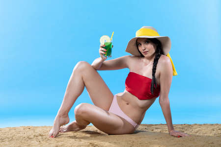 During hot summer, the teenager with a hat on her head holds an alcoholic drink in her hand.の写真素材