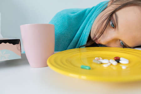 Many tablets and antibiotics to swallow lie prepared on a plate in front of the teen's nose.の写真素材