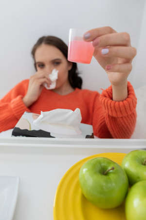 The medicine in a small cup. He is sitting on his bed. A sick teenager. A deep cold.