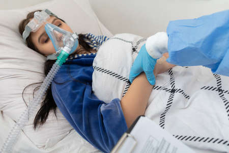Checks blood pulse. Infectious ward physician. A young teenager is lying in a hospital bed.