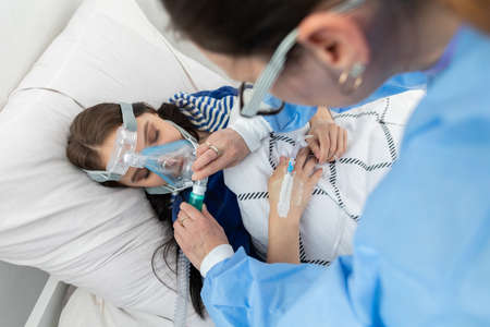 The doctor controls the connection of the ventilator. The teenager lies on a hospital bed. Oxygen...