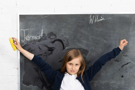 The student, while wiping the chalkboard, raised her hands and turned toward the students in the classroomの写真素材