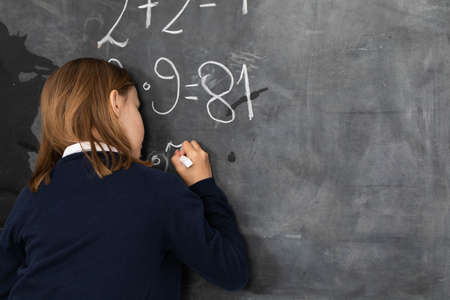 He writes on the chalkboard with chalk. Math problem. A girl at the chalkboard.の写真素材