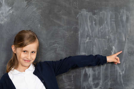 A girl stands smiling at a chalkboard and points to an empty space ready for writing with chalk.の写真素材