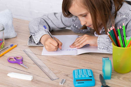 The schoolgirl solves the task. The girl writes in a notebook with a pen. Primary school.