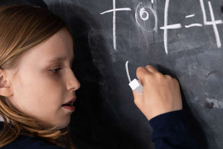 He writes on the chalkboard with chalk. Math problem. A girl at the chalkboard.
