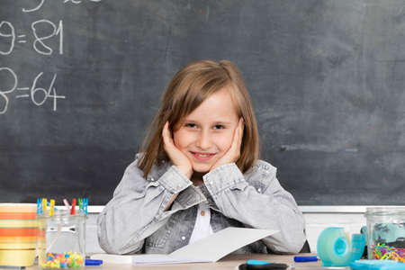 A young schoolgirl is sitting in the classroom. The girl supports her head with her hands. Is...