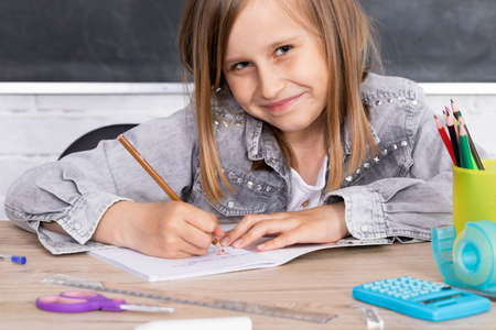 The girl in the lesson was given the task of drawing a teddy bear. The young schoolgirl draws with crayons in a school notebook.の写真素材