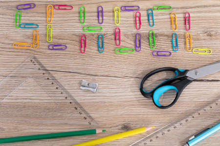 Colorful office paper clips. Inscription school. White school chalk. Wooden school bench top. School...
