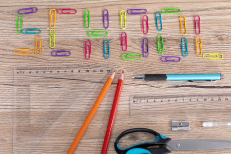Colorful office paper clips. Inscription school. White school chalk. Wooden school bench top. School...