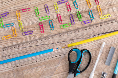 Colorful office paper clips. Inscription school. White school chalk. Wooden school bench top. School accessories.の写真素材
