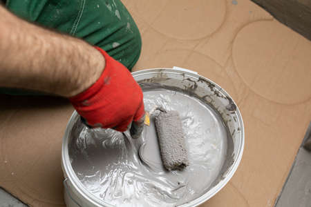 A professional construction worker soaks a paint roller in a bucket full of liquid moisture insulation. During work. Close-up view.の写真素材