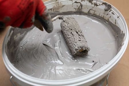 A professional construction worker soaks a paint roller in a bucket full of liquid moisture...