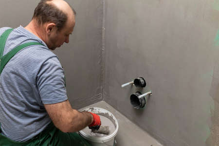 A construction worker soaks a paint roller in a bucket full of liquid moisture insulation. During work.の写真素材