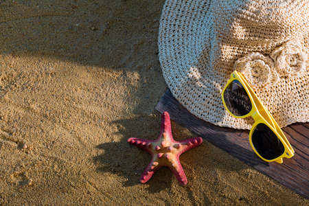 A summer hat and sunglasses lie on the sandy coast of the sea beach.の写真素材