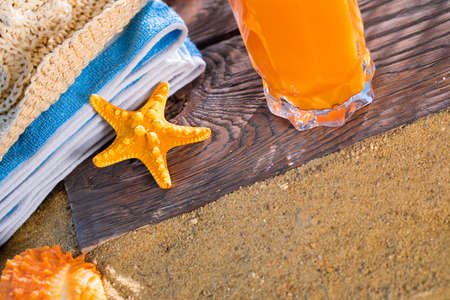 Fresh orange fruit juice stands in a glass with a straw. A beach towel lies on the sandy beach.の写真素材