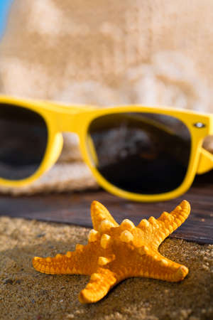 A summer hat and sunglasses lie on the sandy coast of the sea beach.の写真素材