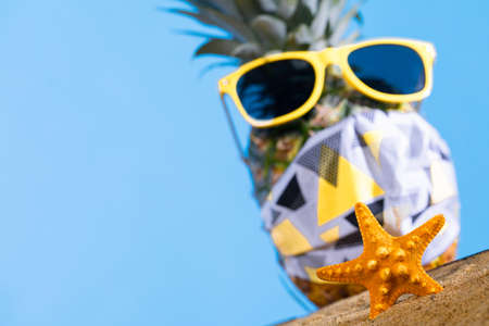 Ripe pineapple. Protective mask. Sunglasses with a yellow frame. Sea beach. Sunny day.の写真素材