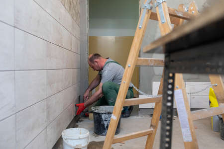 A middle-aged employee deals with laying tiles on the wall in the bathroom. An experienced...
